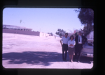 two men and one woman standing beside an automobile on a city street by Haven L. Miller