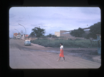 woman walking across a city street, automobile in the background by Haven L. Miller