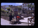 woman, boy and man filling containers with water at city fountain by Haven L. Miller